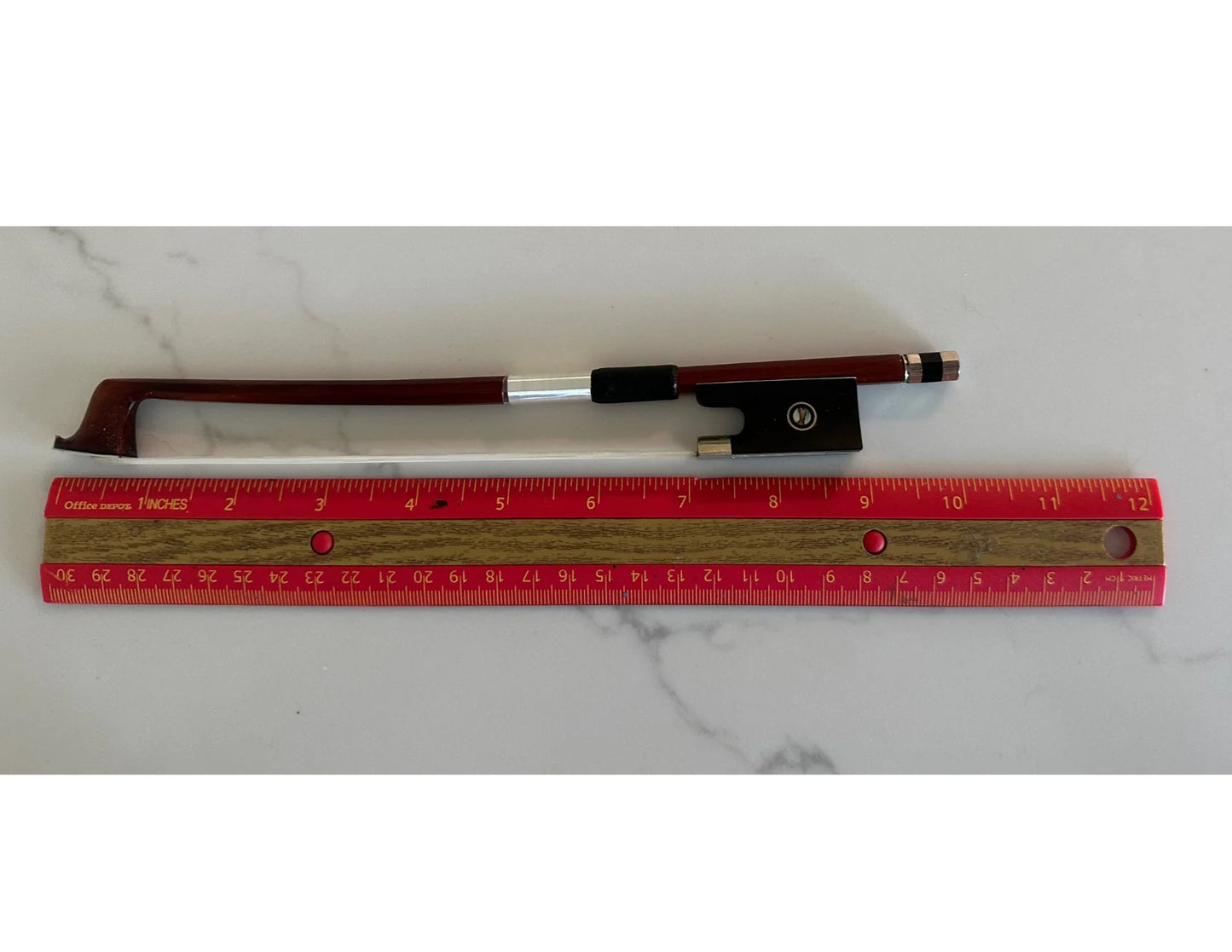 Violin bow with a red ruler for scale on a white marble surface
